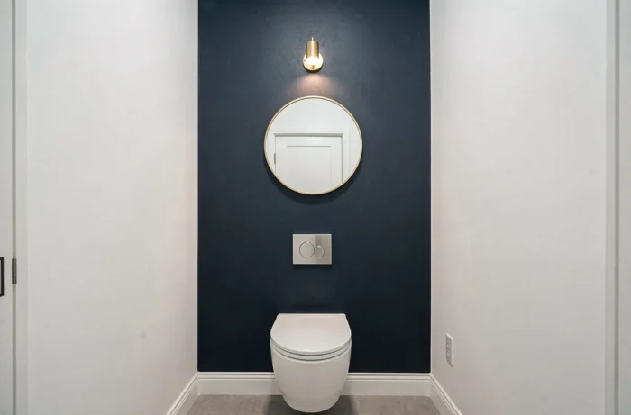 Mur du fond peint en bleu marine foncé effet cocon dans des toilettes suspendues avec miroir laiton